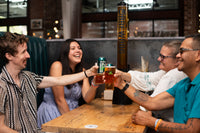 Four people toasting with drinks at a bar.
