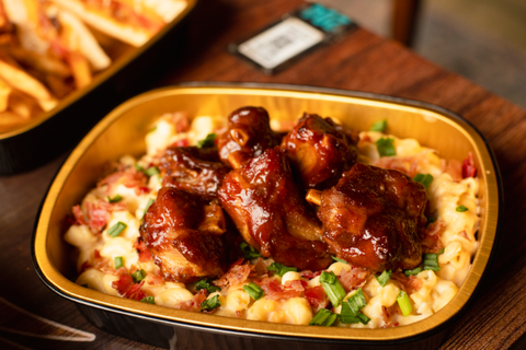 Plated dish of barbecue chicken over macaroni and cheese on a wooden table.