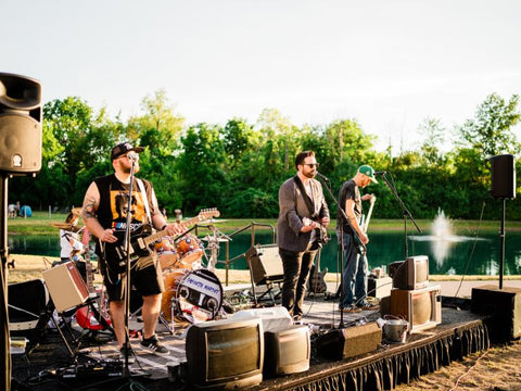Band performing on a stage by a lake with trees in the background