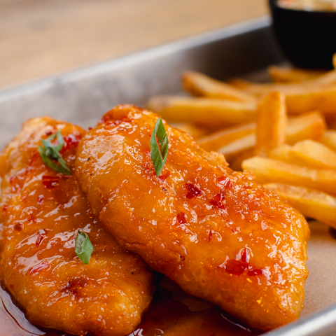 Two pieces of fried fish with a spicy sauce and French fries on a plate.