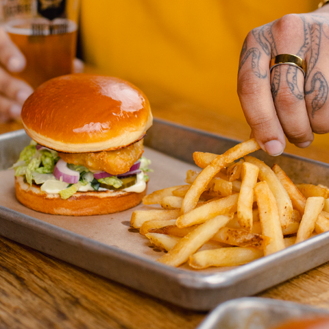 Fish and fries on a tray with a person's hand reaching for the fries.
