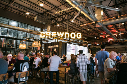 Interior of a BrewDog brewery with patrons and neon sign.