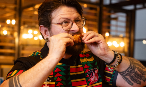 Man eating a piece of fried chicken in a restaurant setting