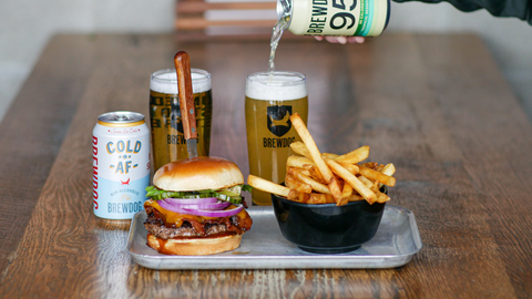 Burger, fries, and beer on a tray with a person pouring a beer bottle.